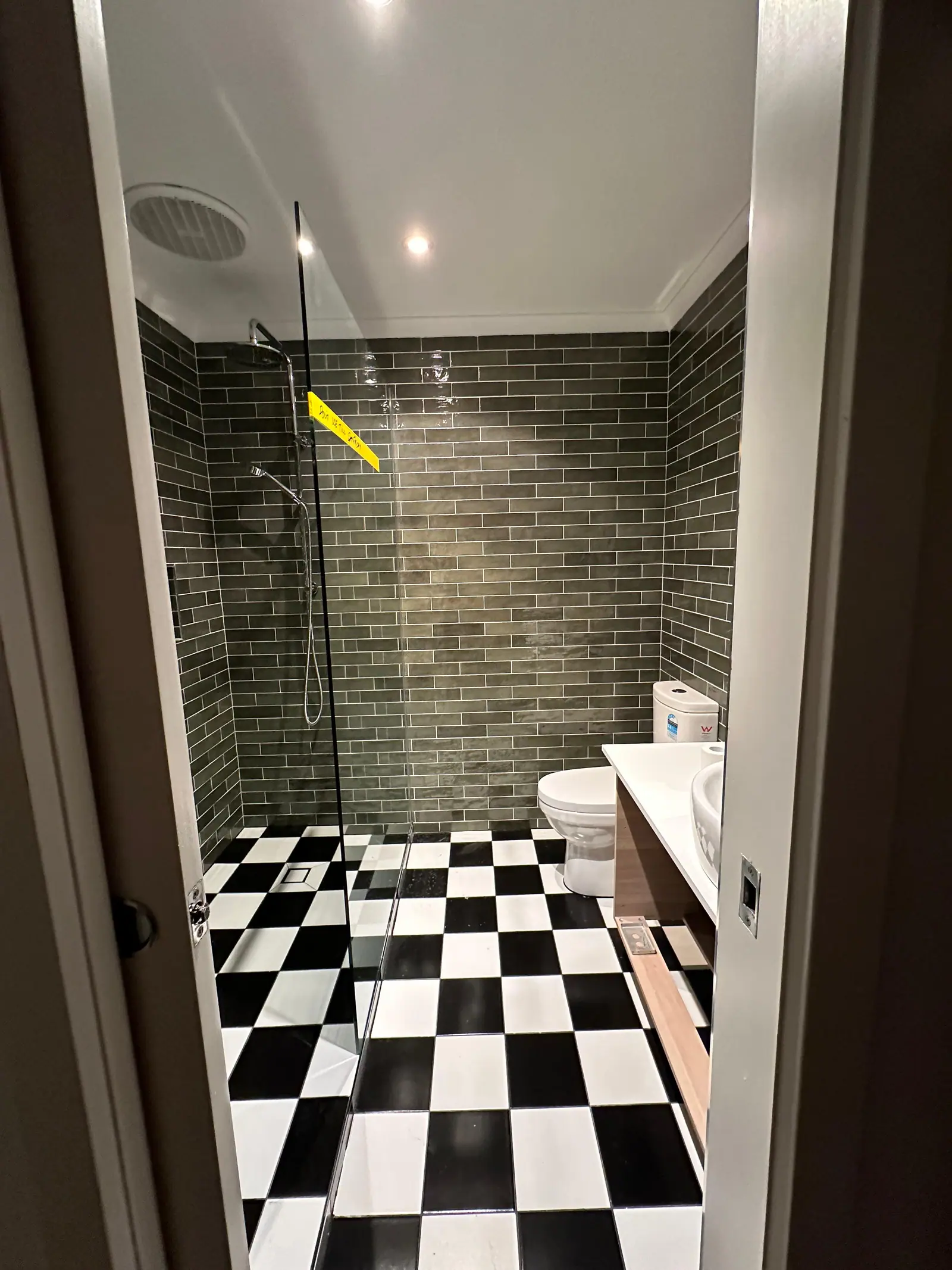 The same bathroom completed, with dark subway wall tiling and a chequered tiled floor