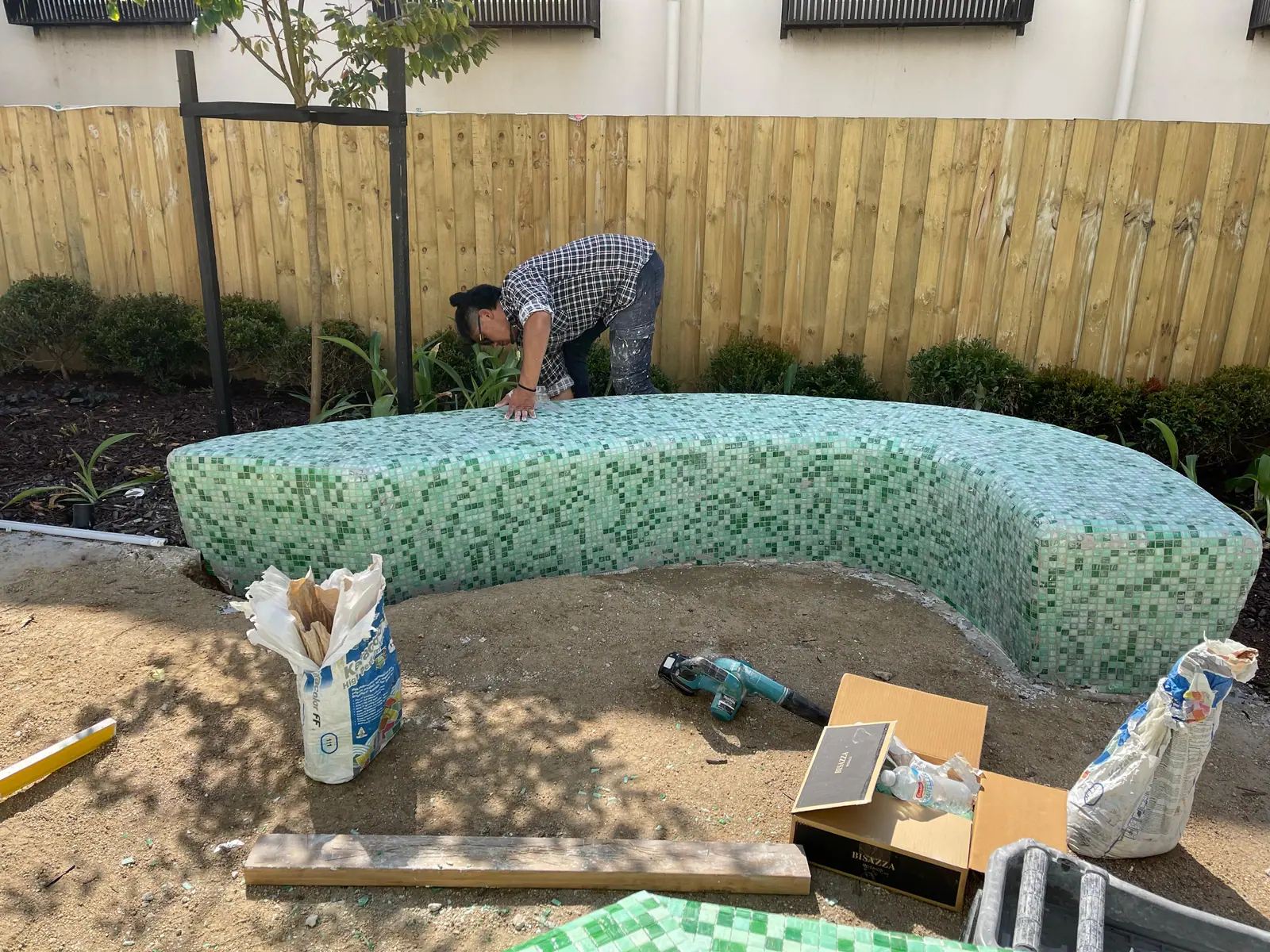 Green mosaic tiles being installed across a curved outdoor seating form