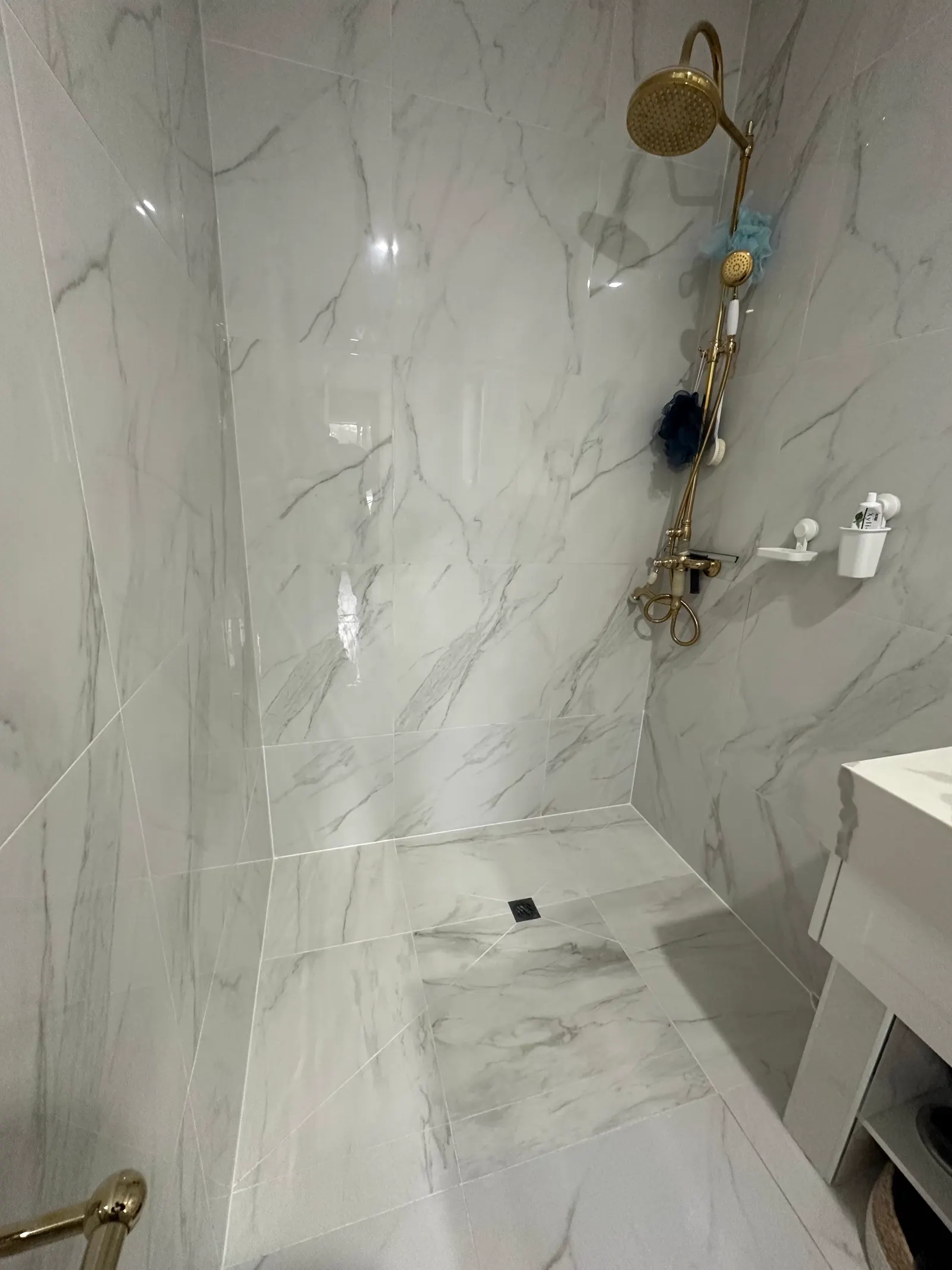 Finished shower lined floor to ceiling in marble-look large-format tile, with an even fall to the central floor waste