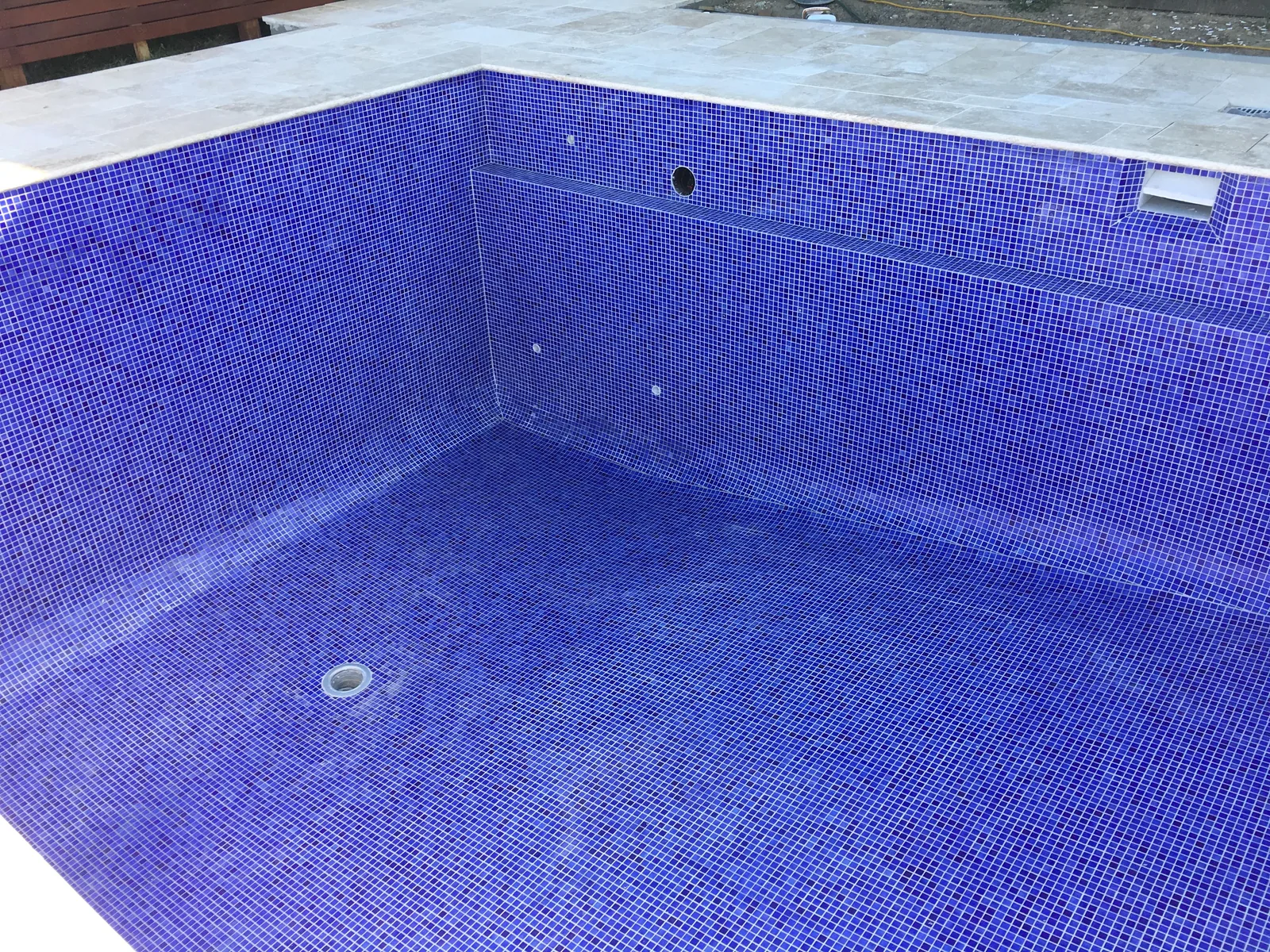 Close view of completed blue and purple mosaic tiling around a pool step and outlet