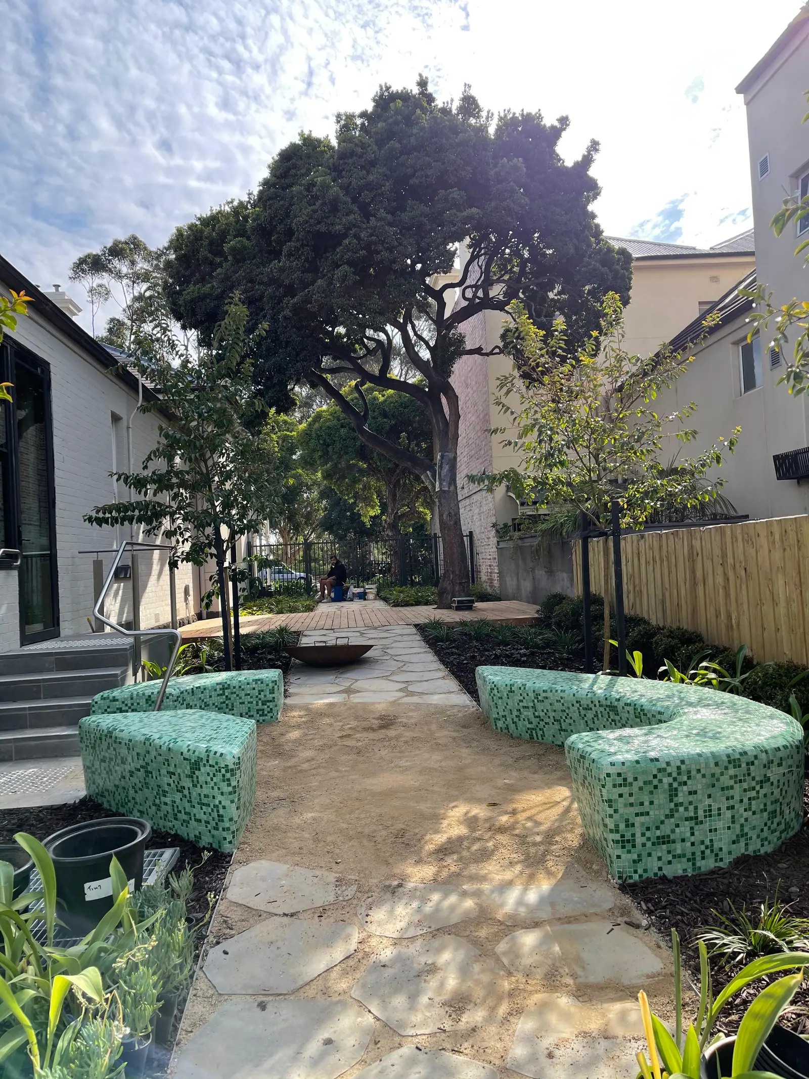 Completed curved outdoor seating finished in green mosaic tiling within a landscaped courtyard