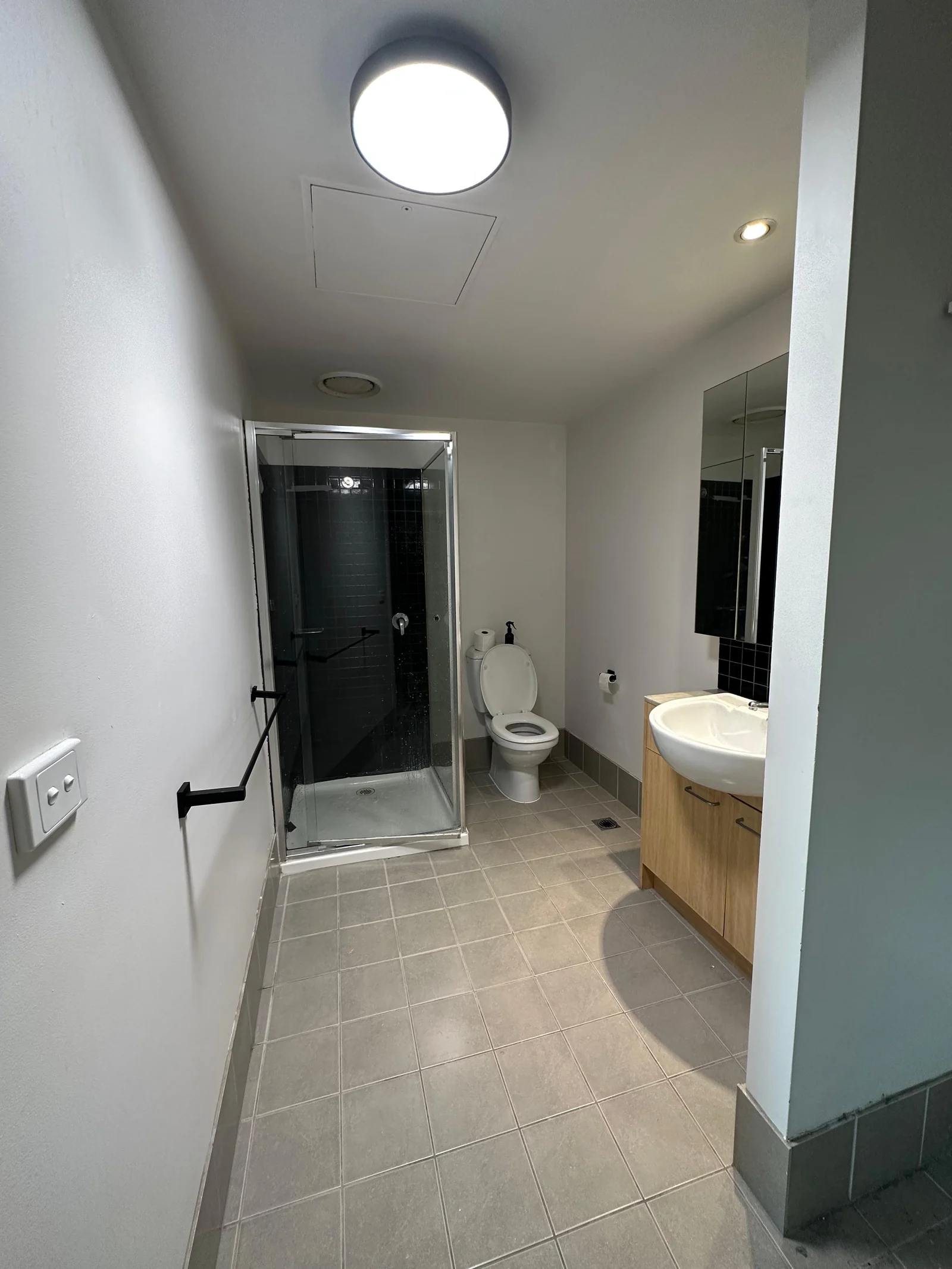 Compact bathroom before renovation, with white walls and grey floor tiles