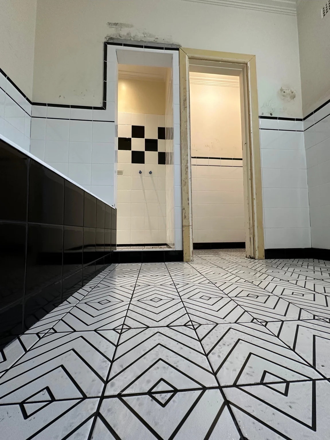 Geometric black and white tiled bathroom floor with contrasting wall tiles before decoration