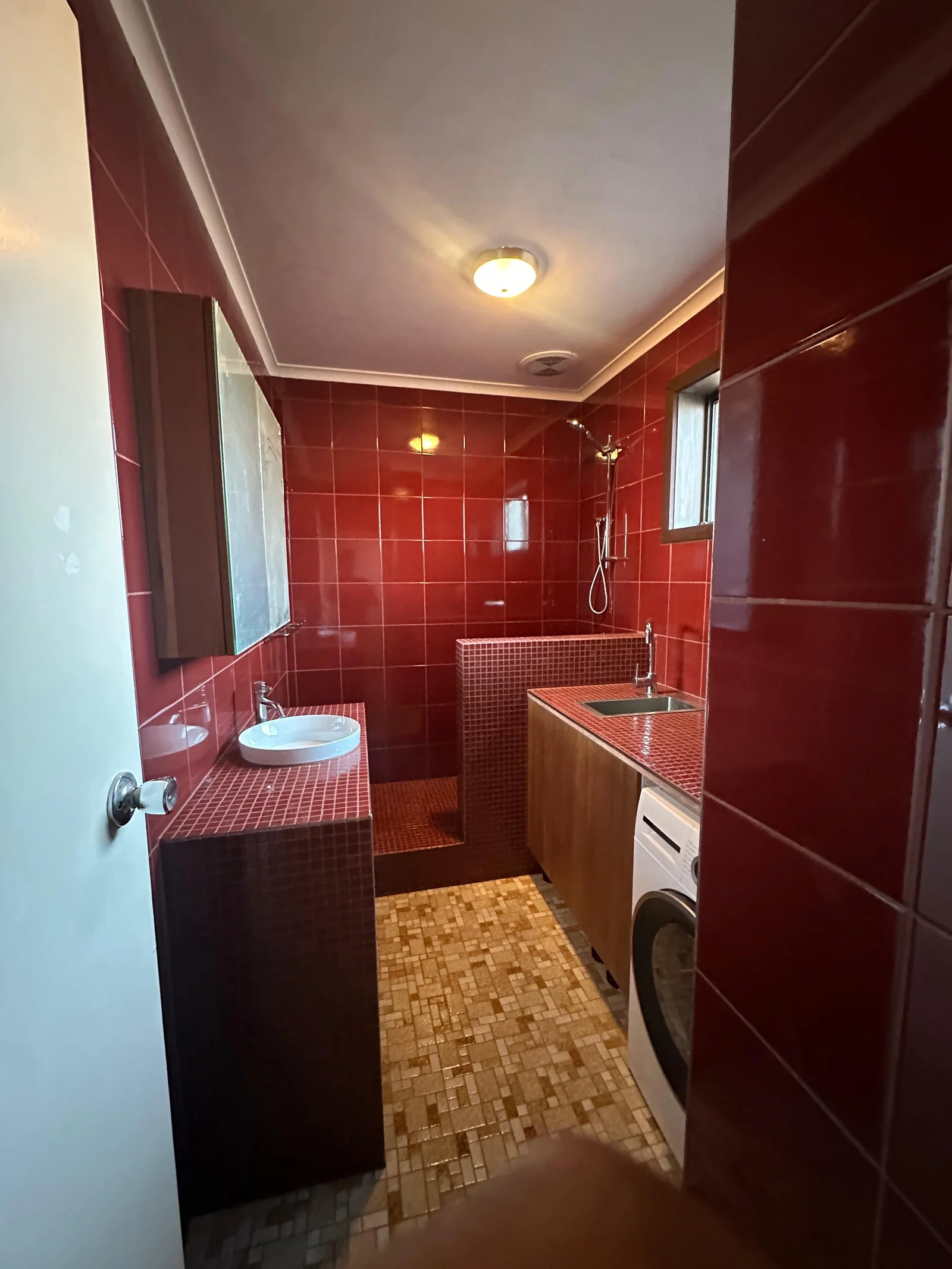 Bathroom after renovation with glossy red wall tiles, mosaic floor and timber cabinetry