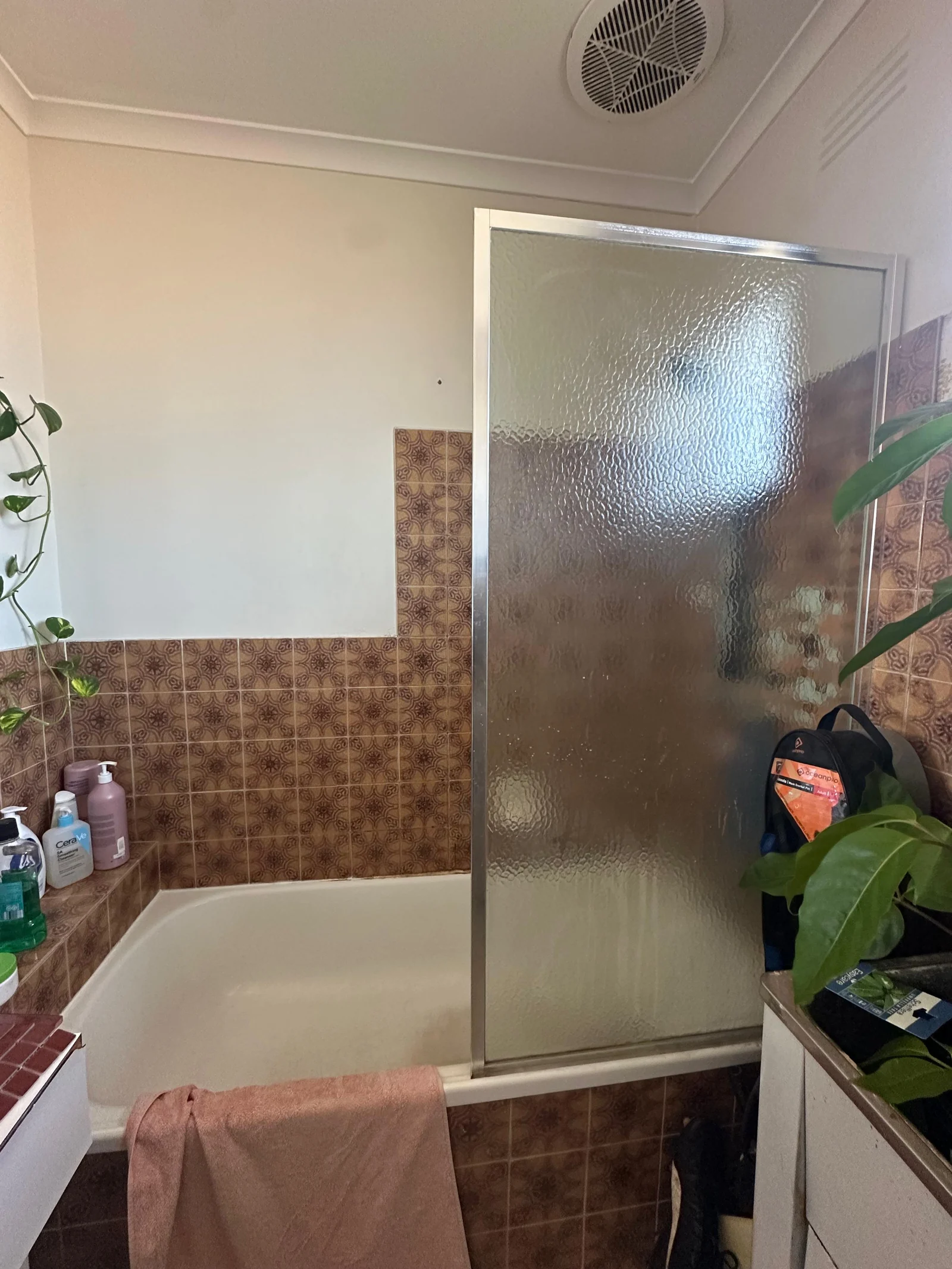 Bathroom before renovation, with brown wall tiles, bath and frosted shower screen