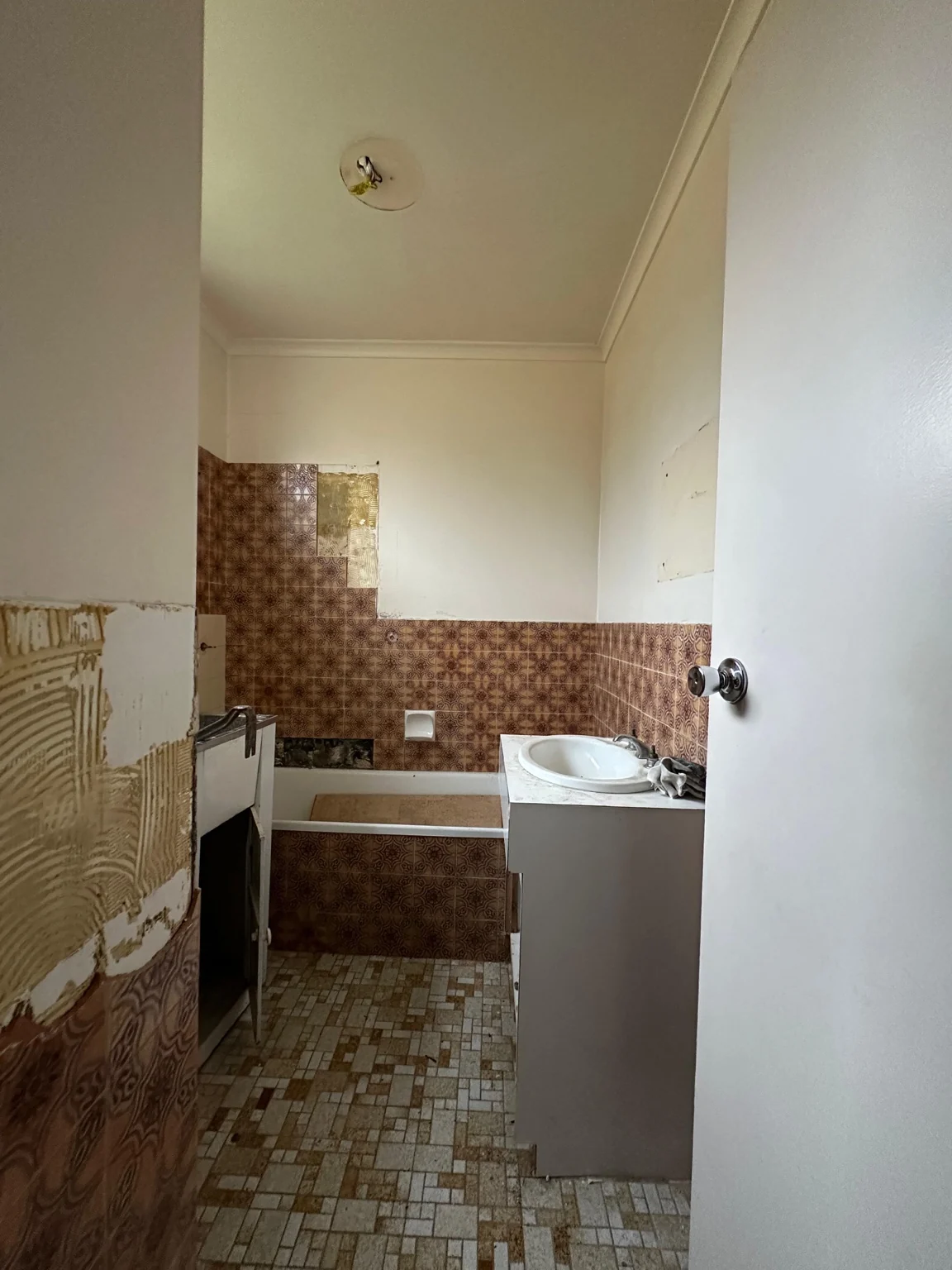 Bathroom before renovation, with old brown wall tiles and partially removed finishes