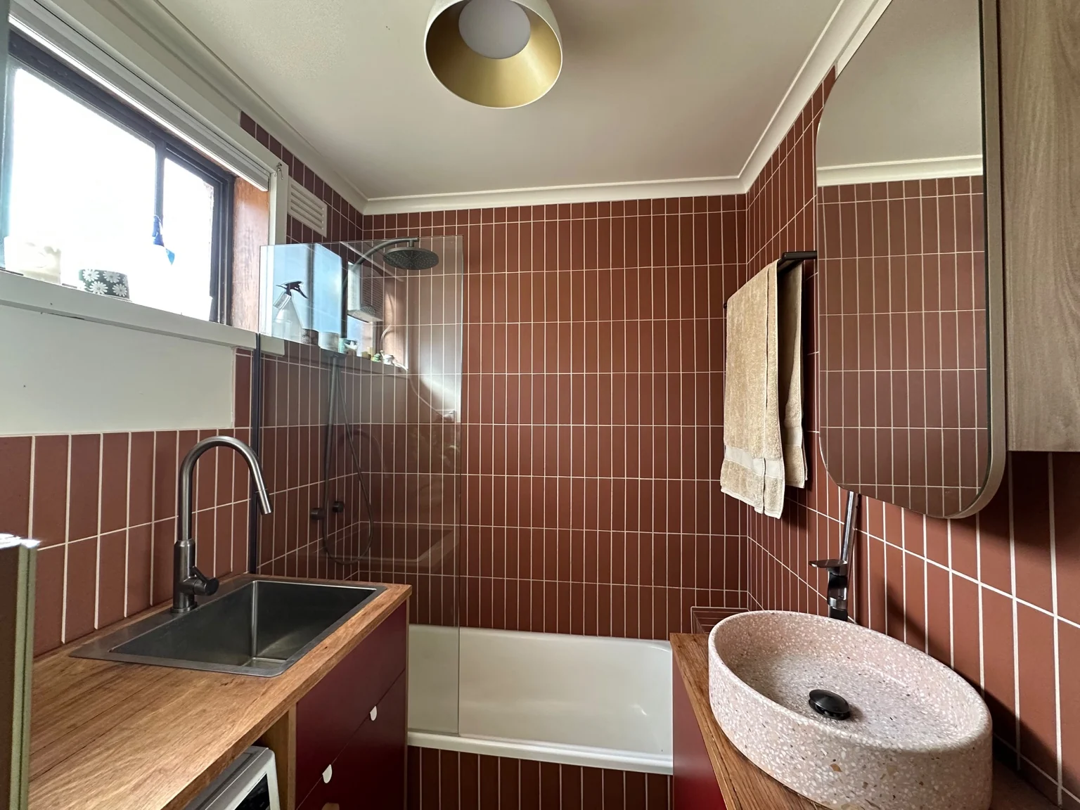 Terracotta tiled bath wall and timber vanity in the renovated bathroom