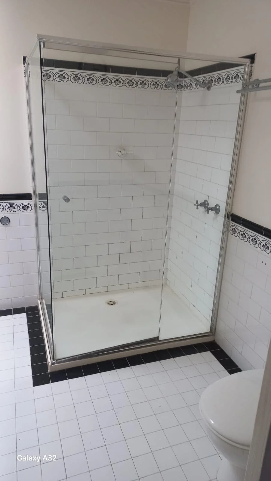 White tiled shower before renovation, with old decorative border and shower screen